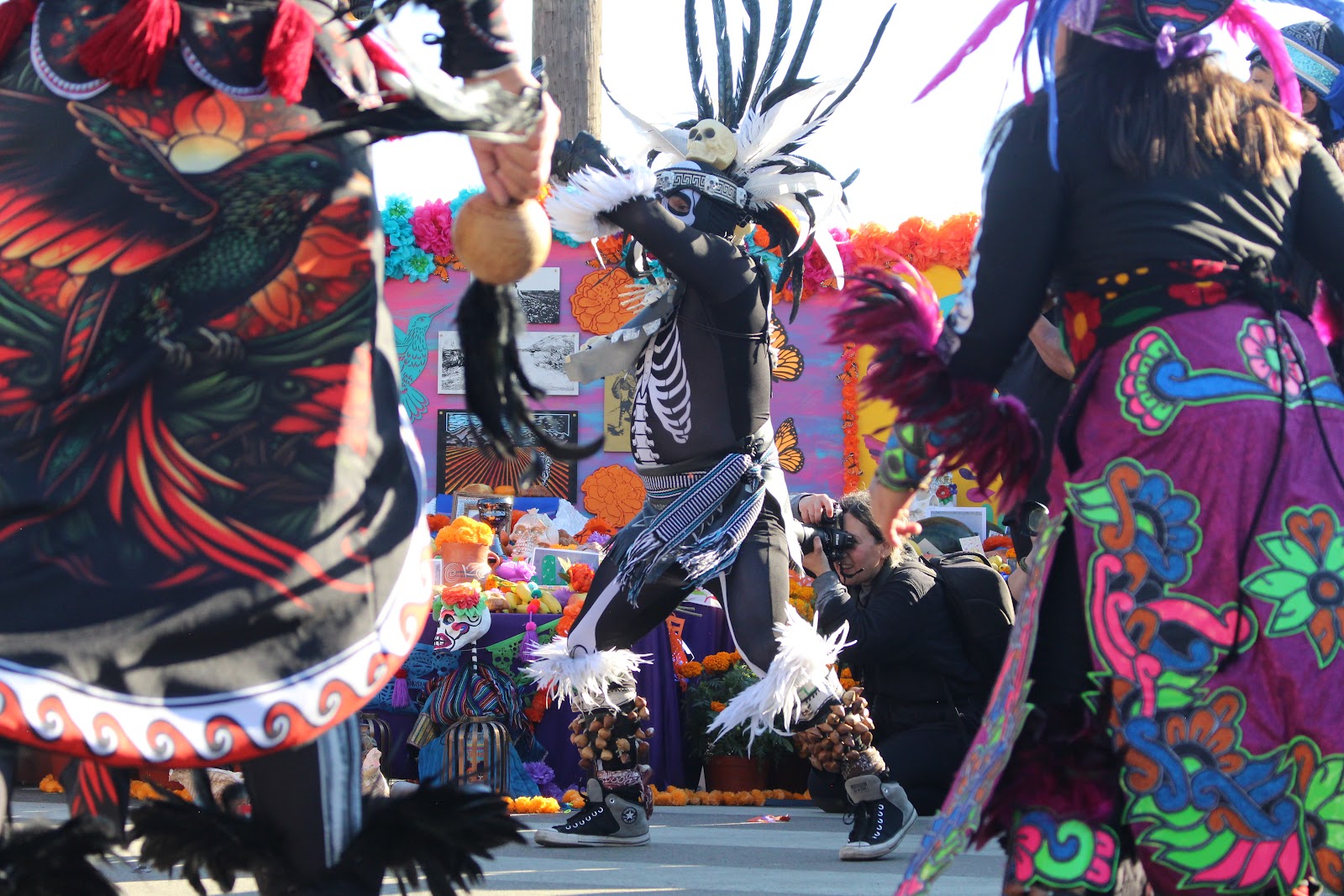 Danzante performers in feathered regalia and skull face paint marching in the procession