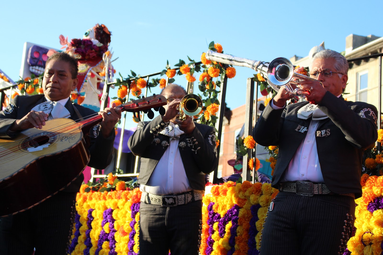 Mariachi musicians in charro suits performing on a float draped with marigolds